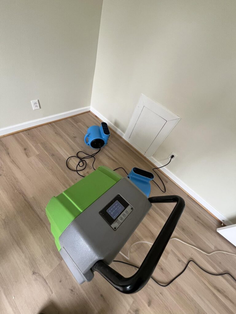 Dehumidifier and air mover running near a wall access panel during daily moisture monitoring in a Bellingham, WA home