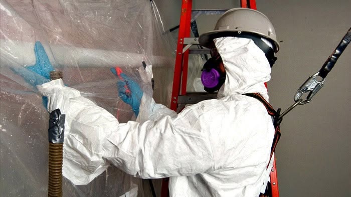 Technician in full PPE and respirator sealing a plastic containment barrier during mold remediation in Bellingham, WA